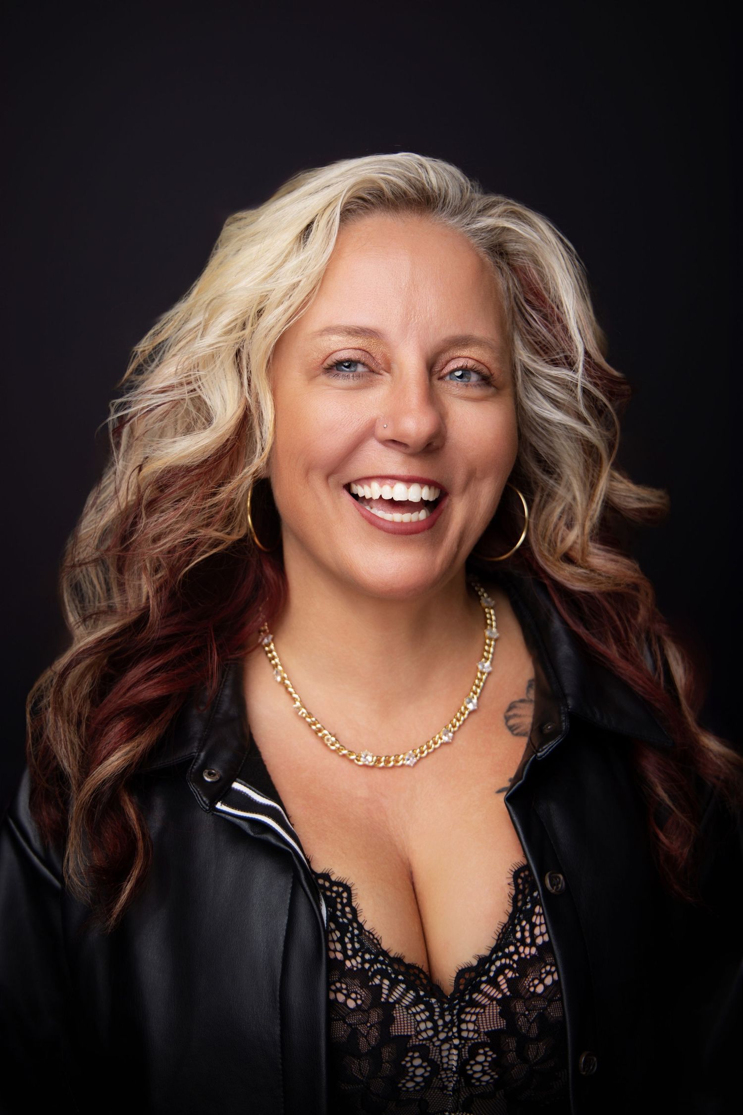 Smiling woman with blonde and burgundy hair wears black lace and a gold necklace, captured for Sassi Frass Boutique by Carolina Waldroff