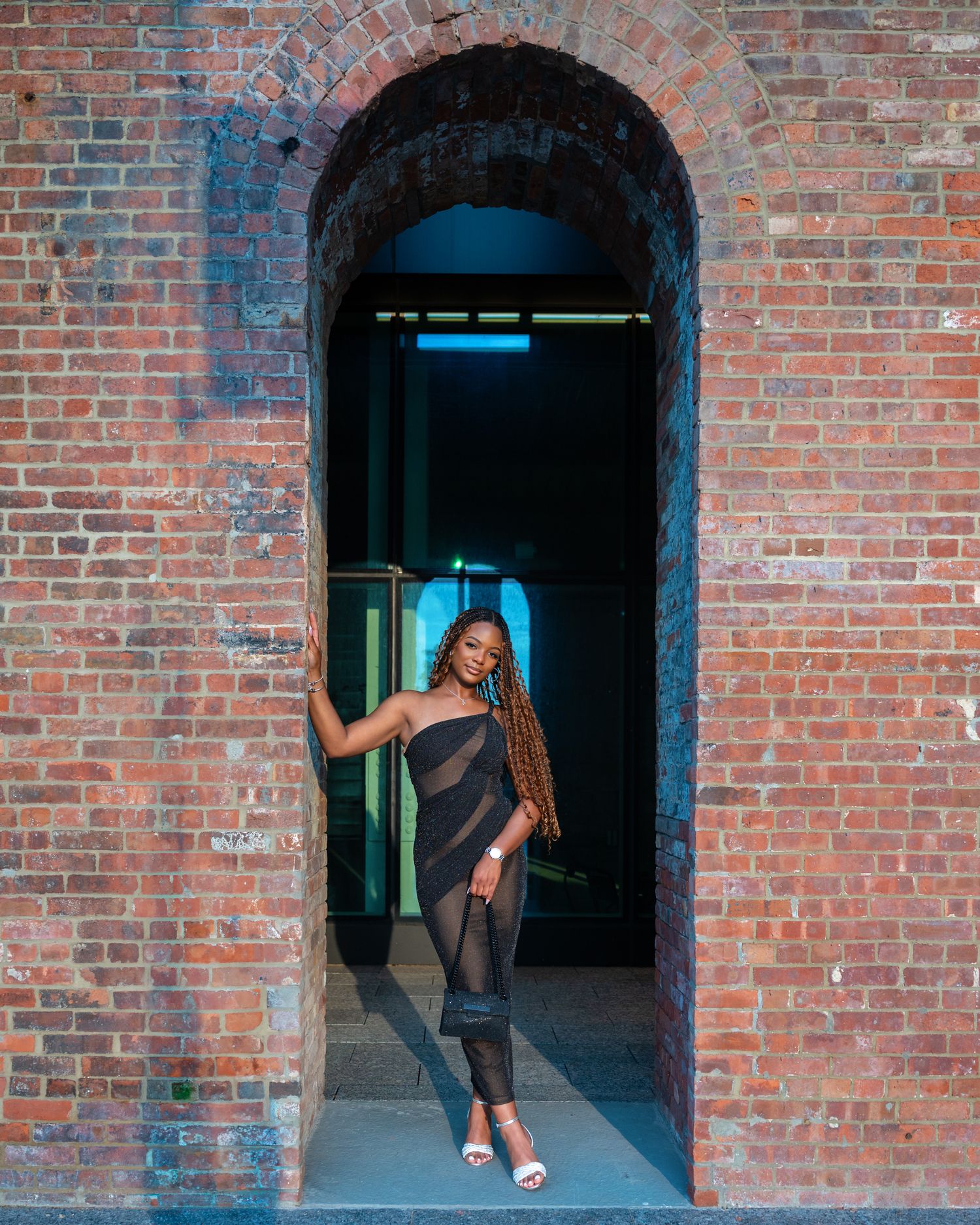 Stylish figure poses in an arched brick doorway illuminated by blue lighting at night.