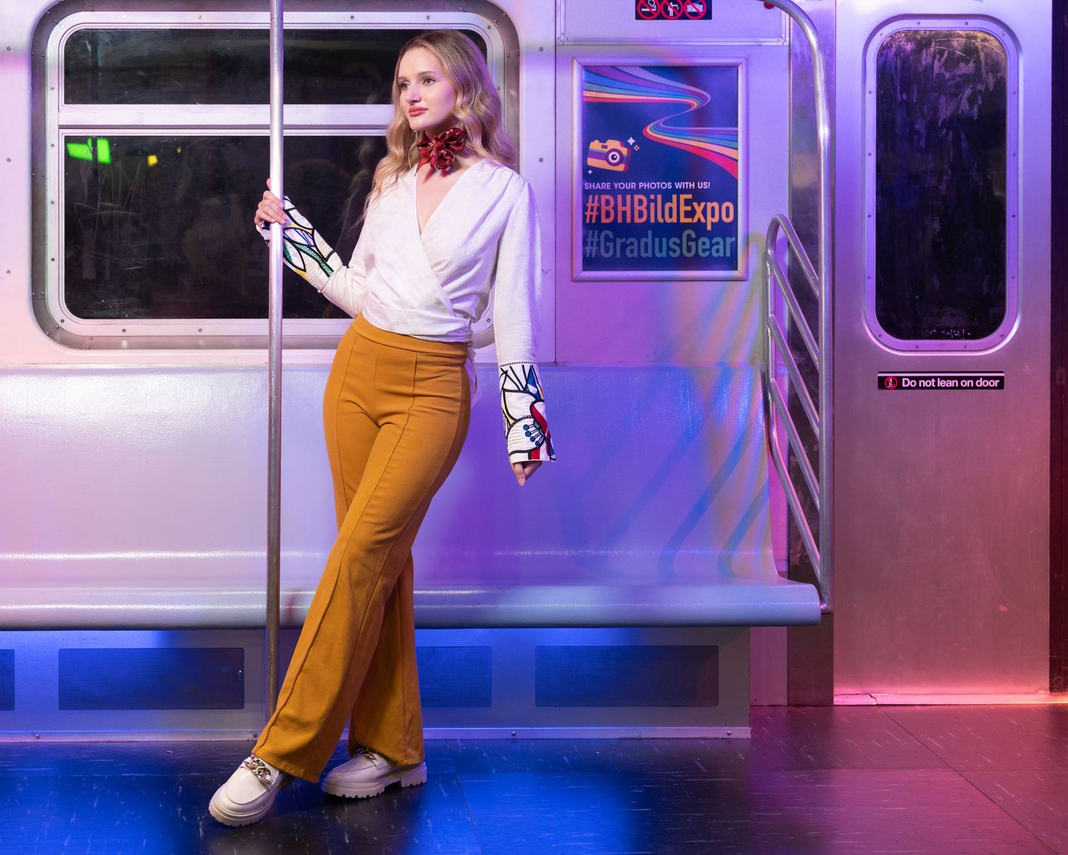 Figure in a white top and yellow pants poses against a subway car interior with purple lighting effects.
