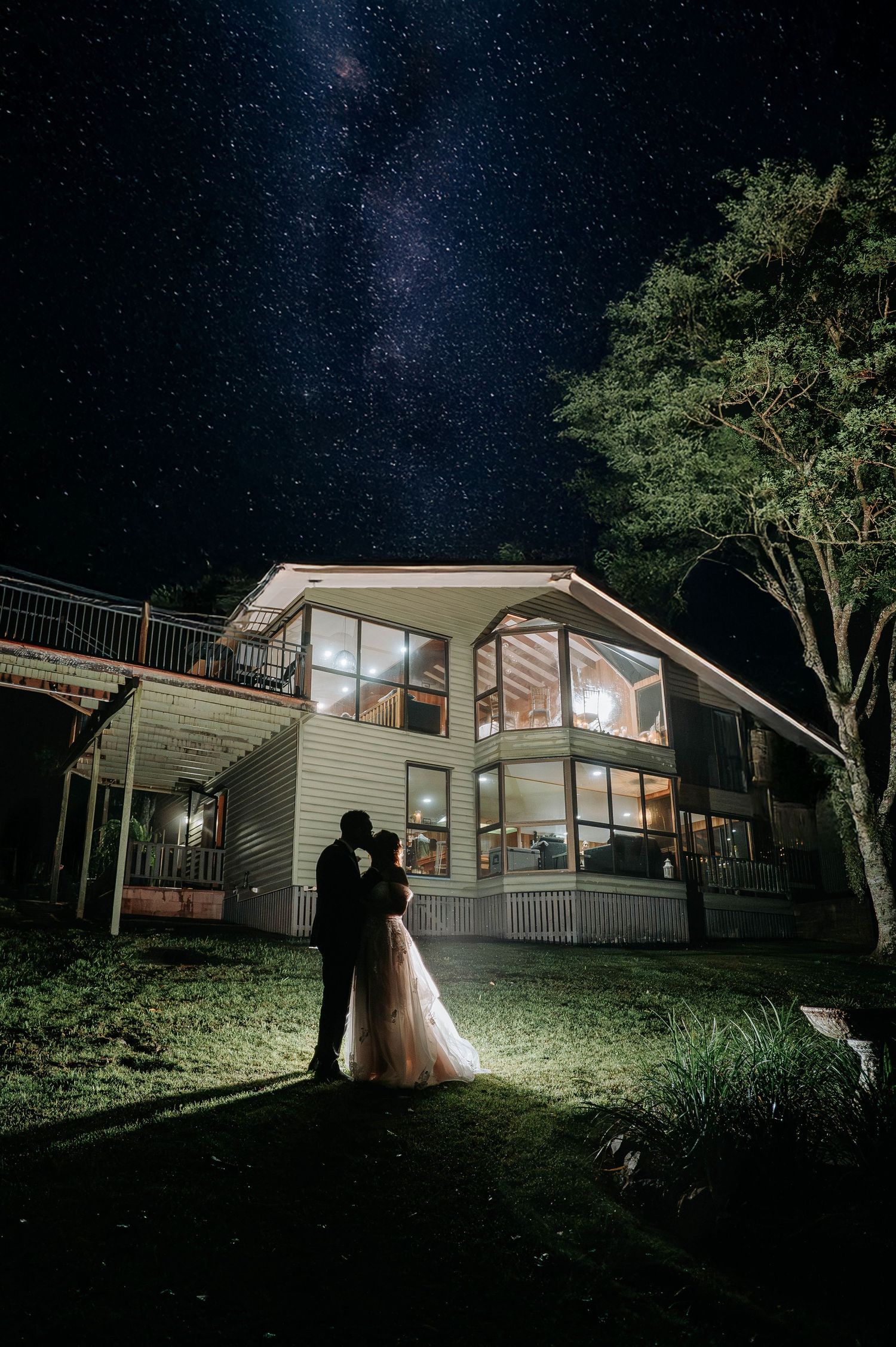 Silhouette of couple under starry night sky in front of modern house with large windows.