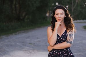 A woman in a navy floral dress poses thoughtfully on a scenic country road at dusk.