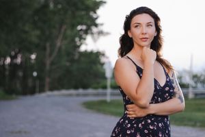 Person in a floral dress stands thoughtfully on a curved path with trees in the background during golden hour.