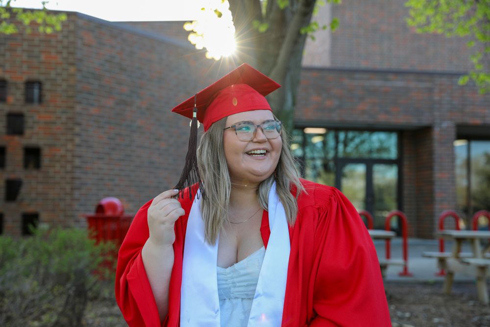 Joyful graduate in red regalia poses outside brick building during golden hour.