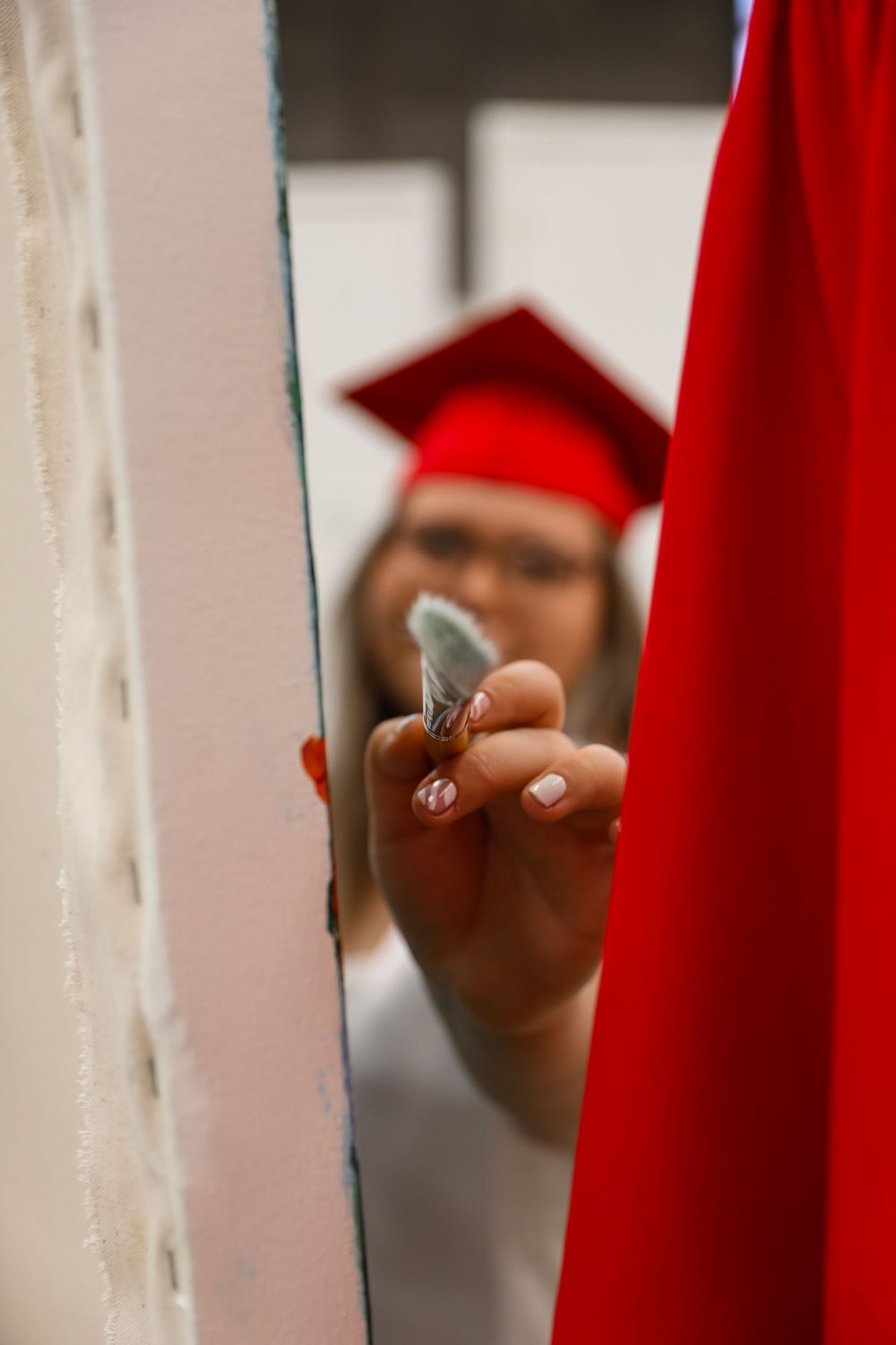 Hand holding nail polish through a gap while wearing red graduation attire.