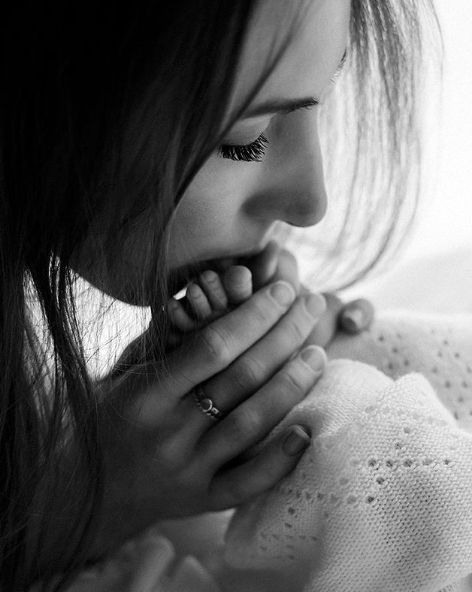 Black and white portrait showing a person in a pensive moment with hands covering mouth, wearing a white lace garment.