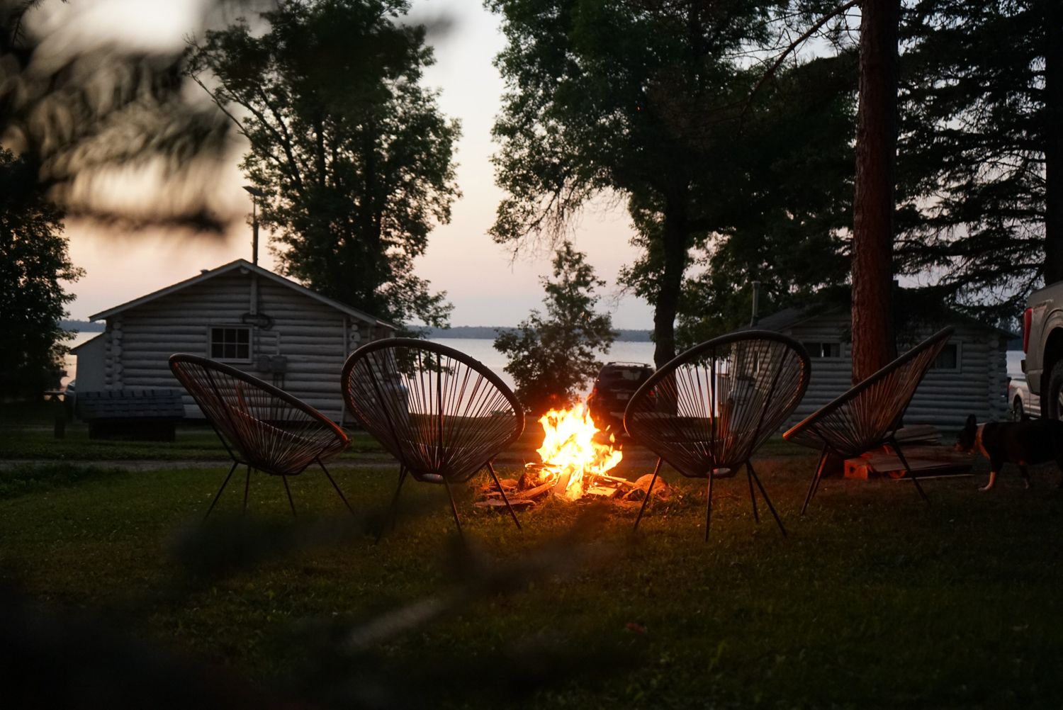 Sunset over a lakeside campsite with chairs silhouetted against the orange sky.