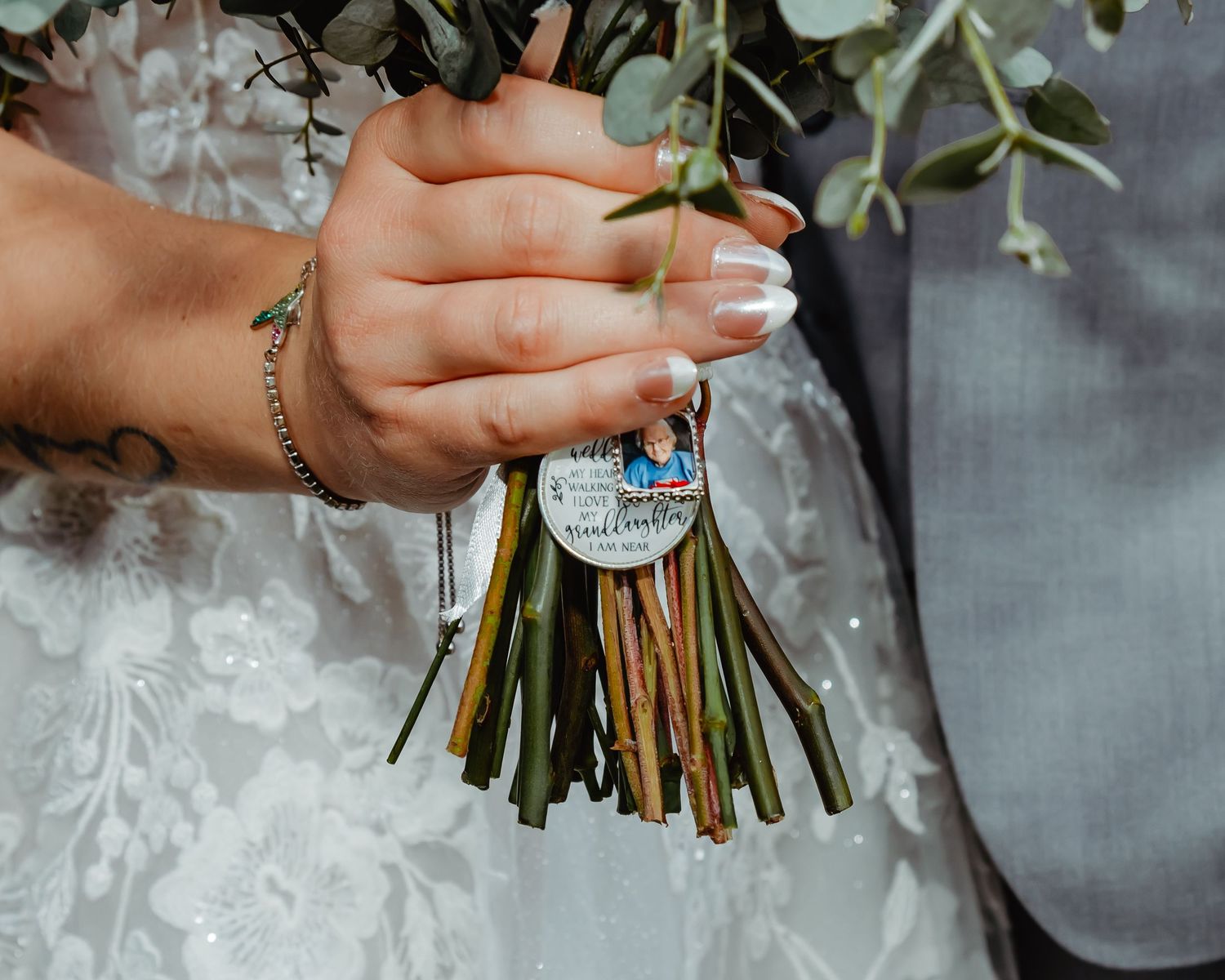 Close-up view of hands holding a wedding bouquet with a memorial charm or photo locket attached to the stems.