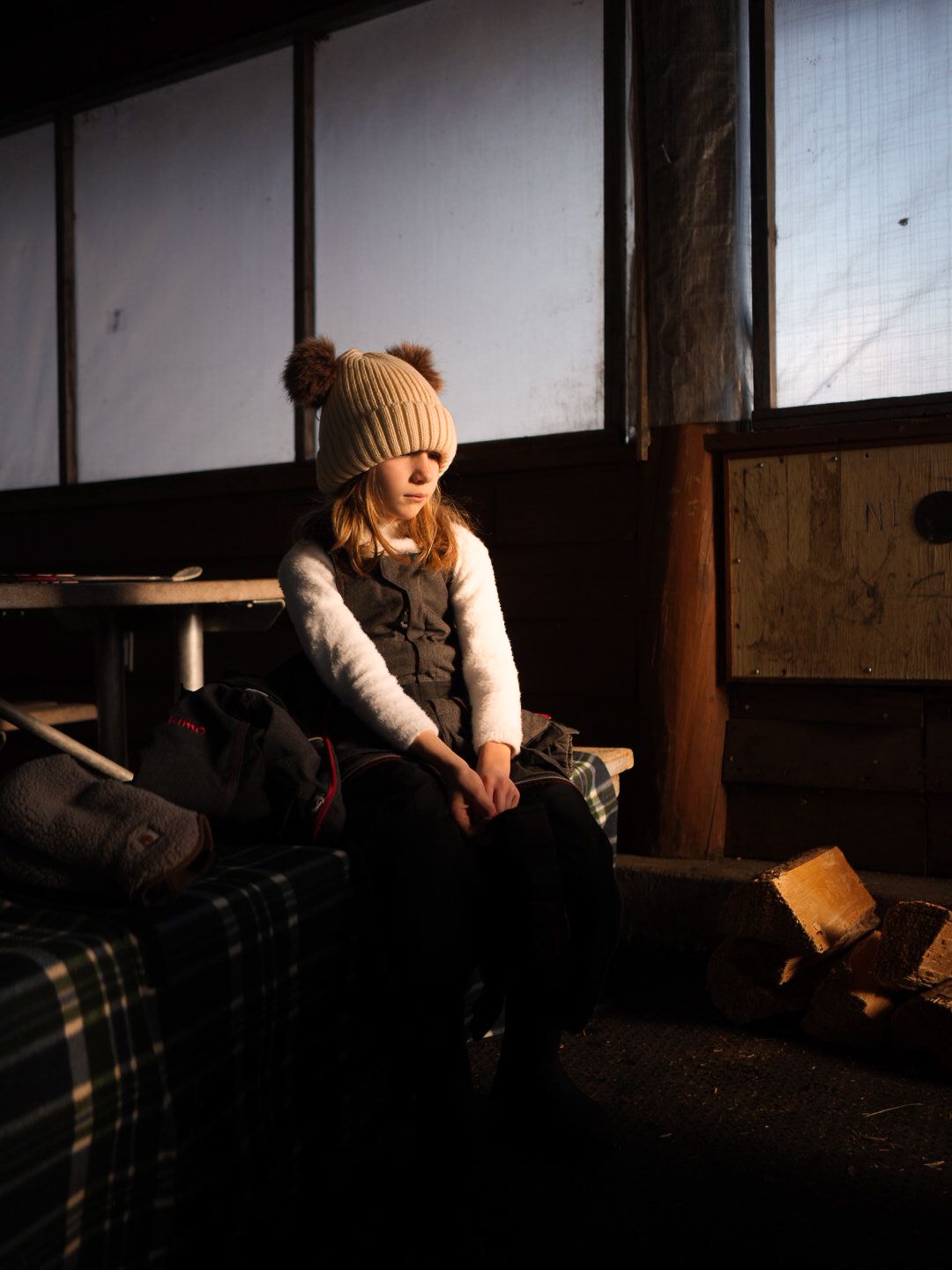 Person in a knit beanie and winter clothes sits indoors in moody lighting.