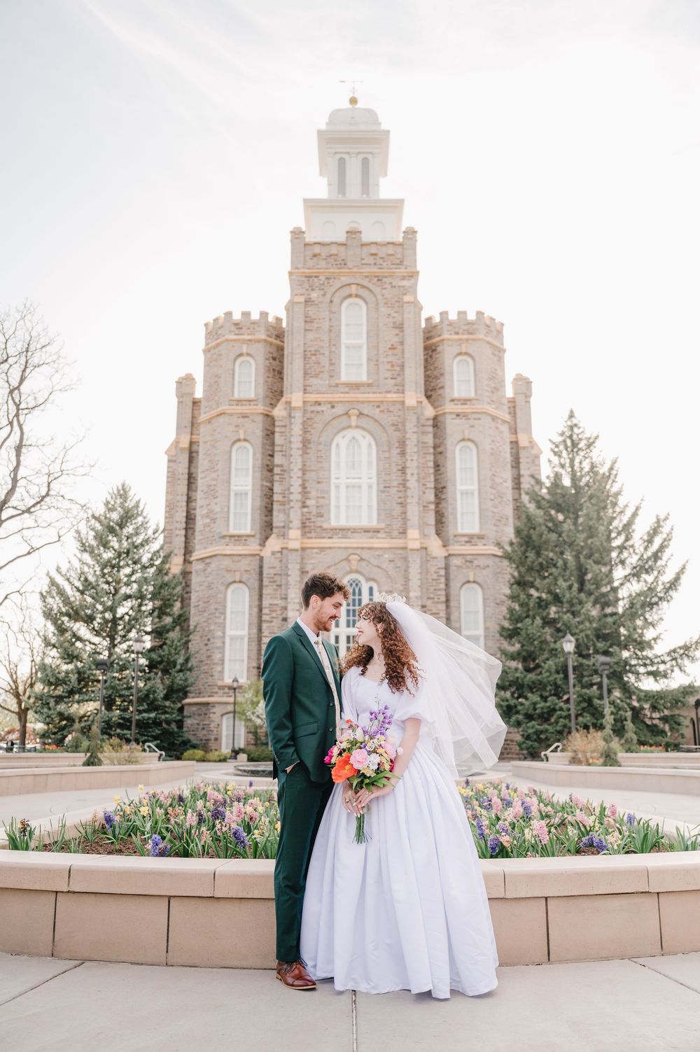 Wedding couple poses in front of a historic stone temple with gothic architecture and spring flowers blooming.