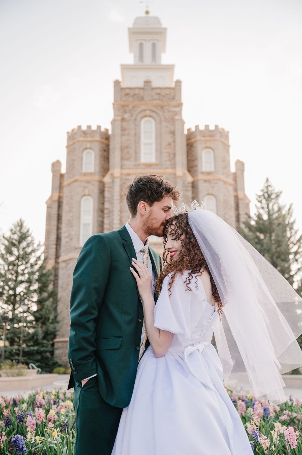 A romantic wedding portrait in front of a beautiful stone temple with arched windows and blooming spring flowers.
