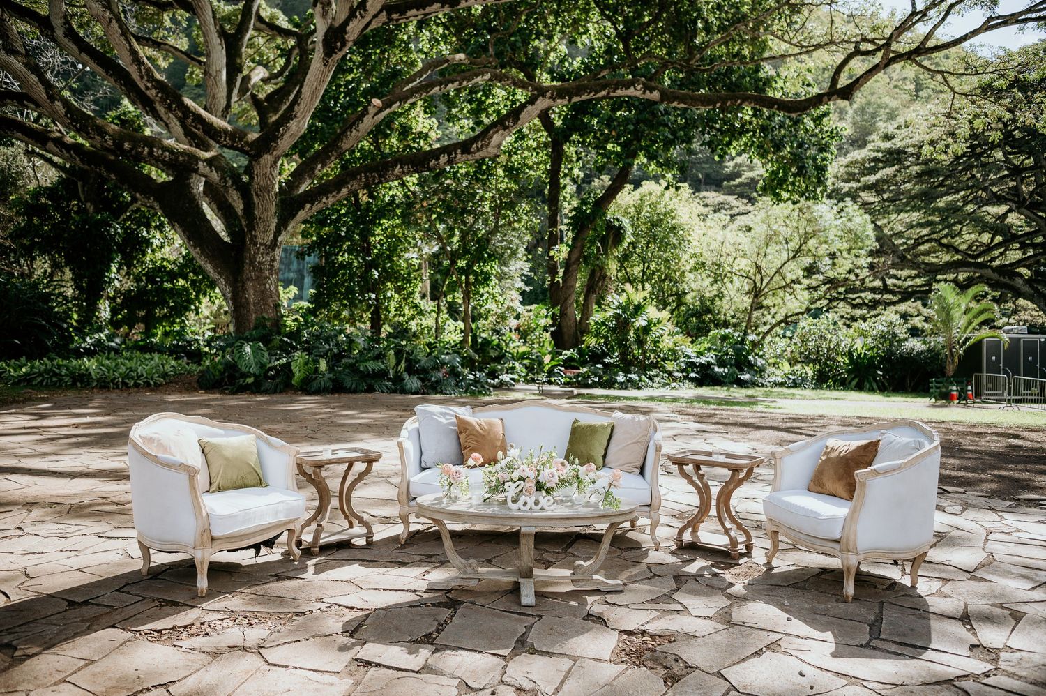 Wedding ceremony taking place outdoors at a scenic waterfall grotto with guests seated on rustic wooden chairs.