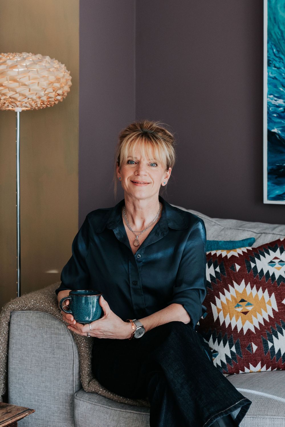 Woman relaxing on gray couch with decorative southwestern pillows and modern lamp in cozy living room interior.