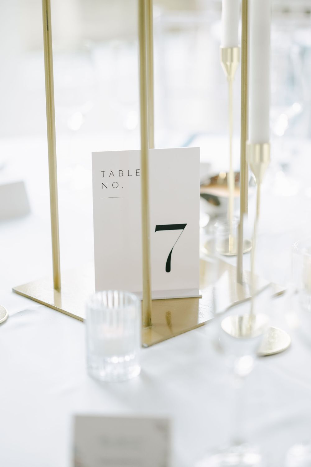 Minimalist white table number card displaying number 7 on an elegant wedding reception table with gold accents.