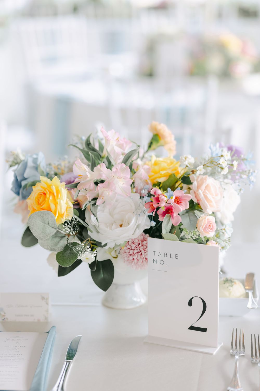 Elegant wedding centerpiece with pastel roses, peonies and greenery in white vase next to table number two card.