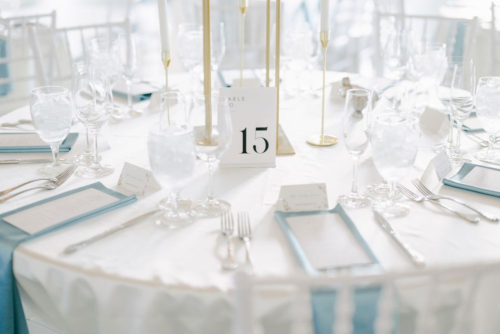 Elegant wedding reception table set in white and blue with table number 15 and crystal glassware.