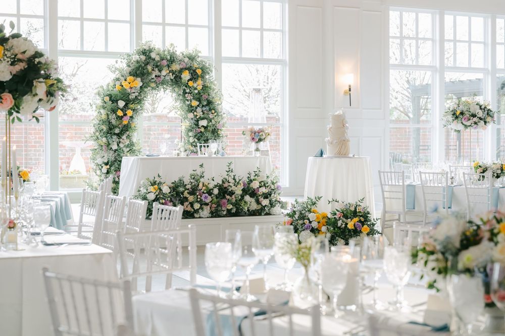 Elegant white wedding reception venue decorated with floral arches and greenery arrangements on round tables.