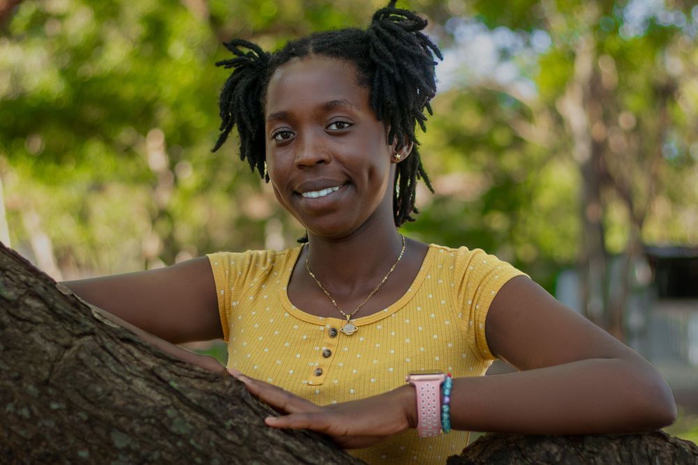 A lady smiling  posing behind a tree trunk