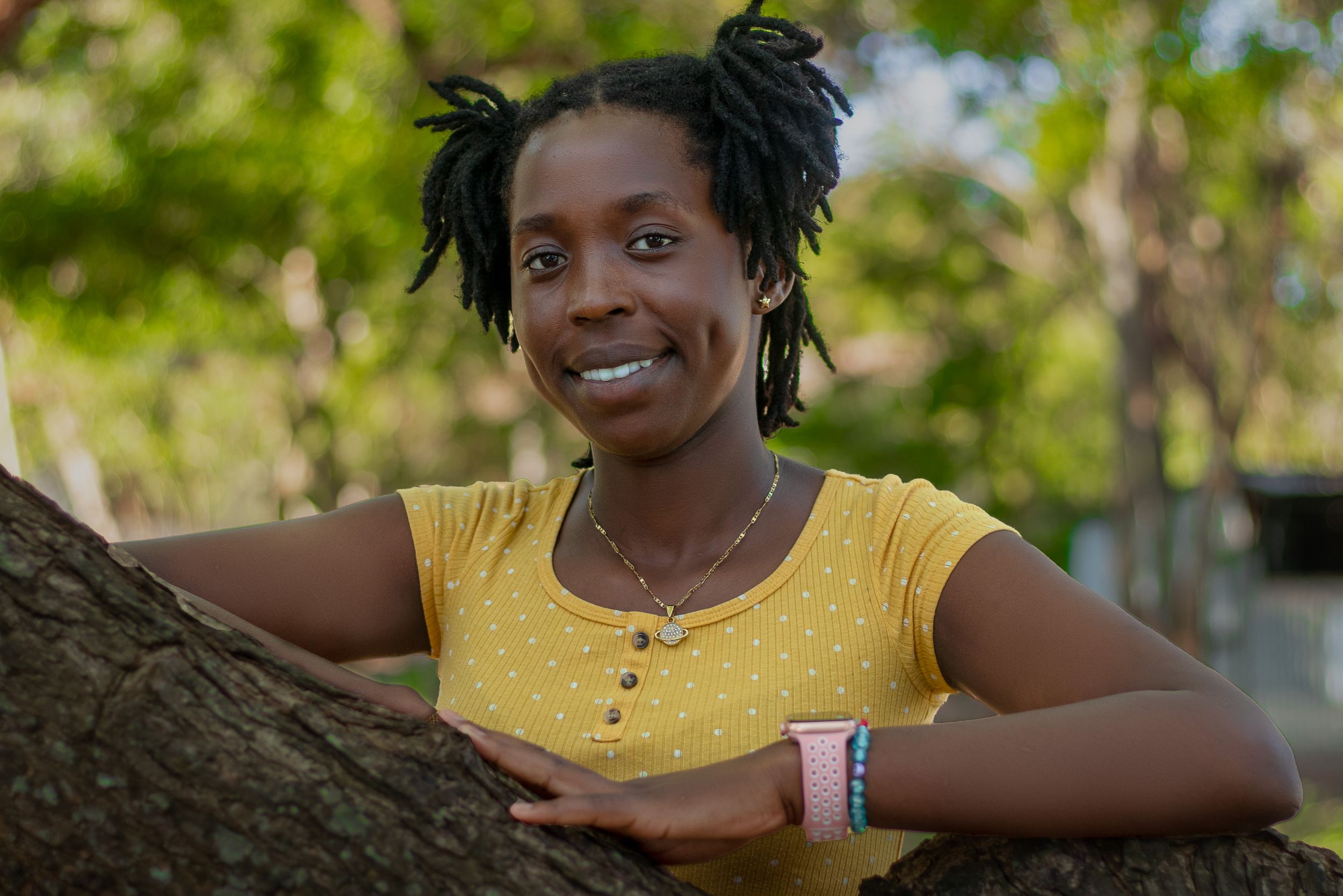 A lady smiling  posing behind a tree trunk