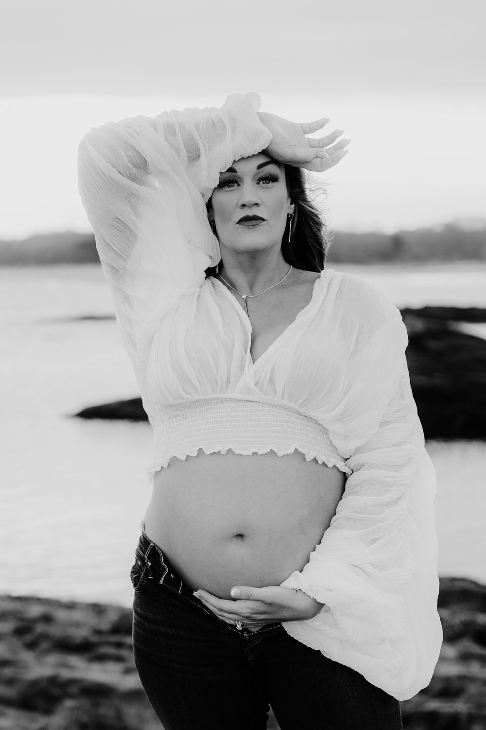 Maternity photoshoot in black and white featuring a white peasant blouse against a coastal backdrop.