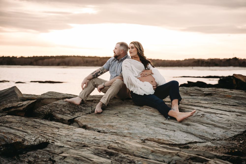 Romantic sunset maternity photos captured on rocky coastal terrain.