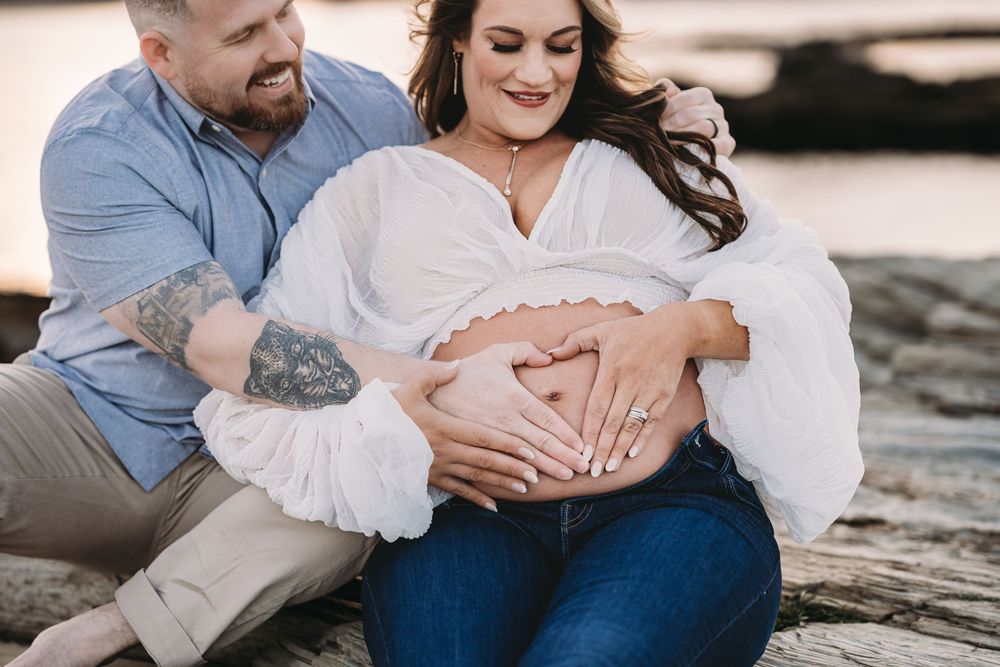 Intimate maternity session photographed on rocky shoreline during golden hour.