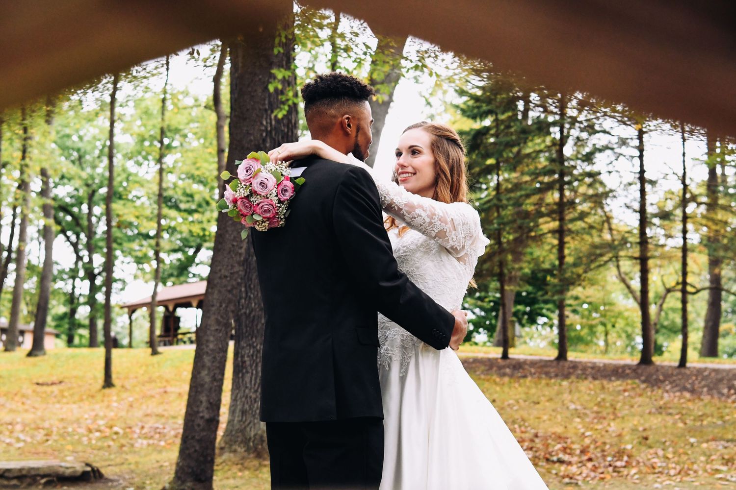 Romantic autumn wedding dance captured between trees with bride holding pink bouquet.