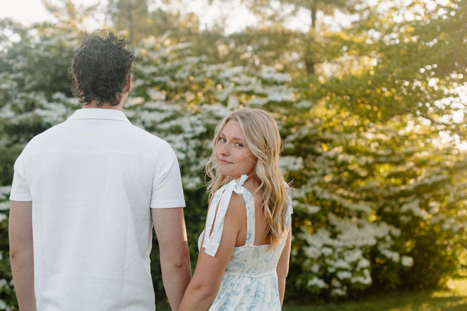 Couple walking away and she is looking back over her shoulder smiling during their engagement session at Millennium Park in Grand Rapids MI.