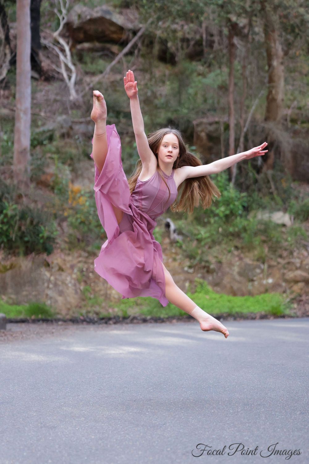 Dancer in pink dress executes graceful leap on outdoor road.