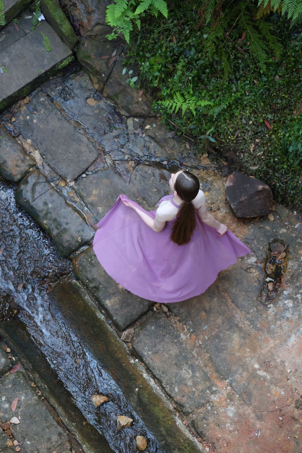 Overhead view of dancer in flowing purple dress on stone steps.