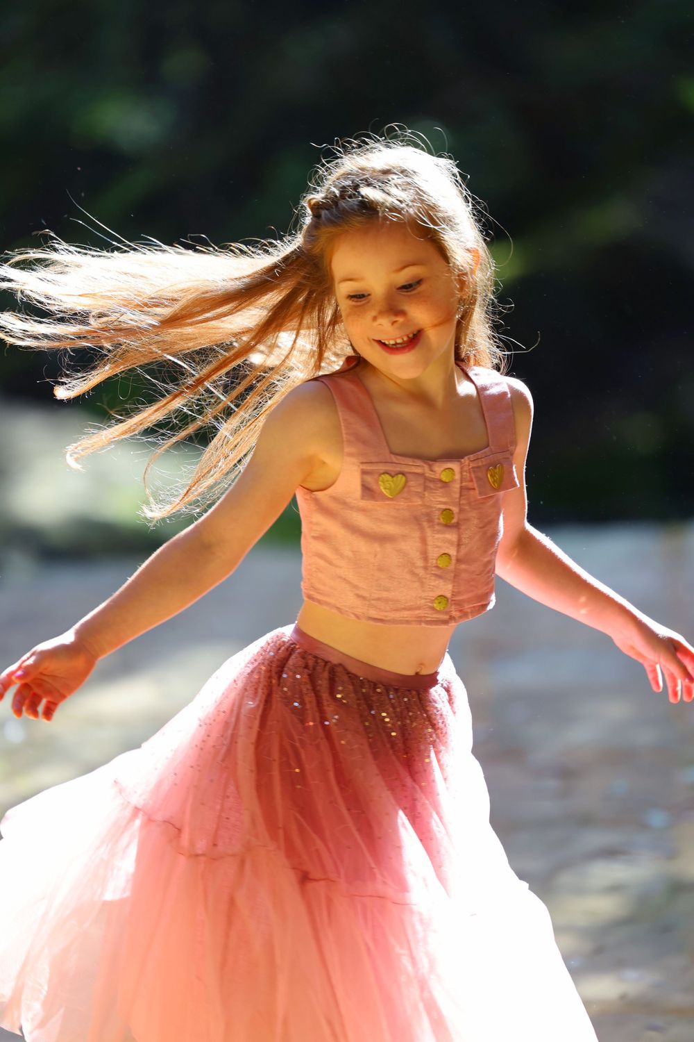 Young dancer in pink tulle skirt twirls joyfully with flowing hair in natural sunlight.