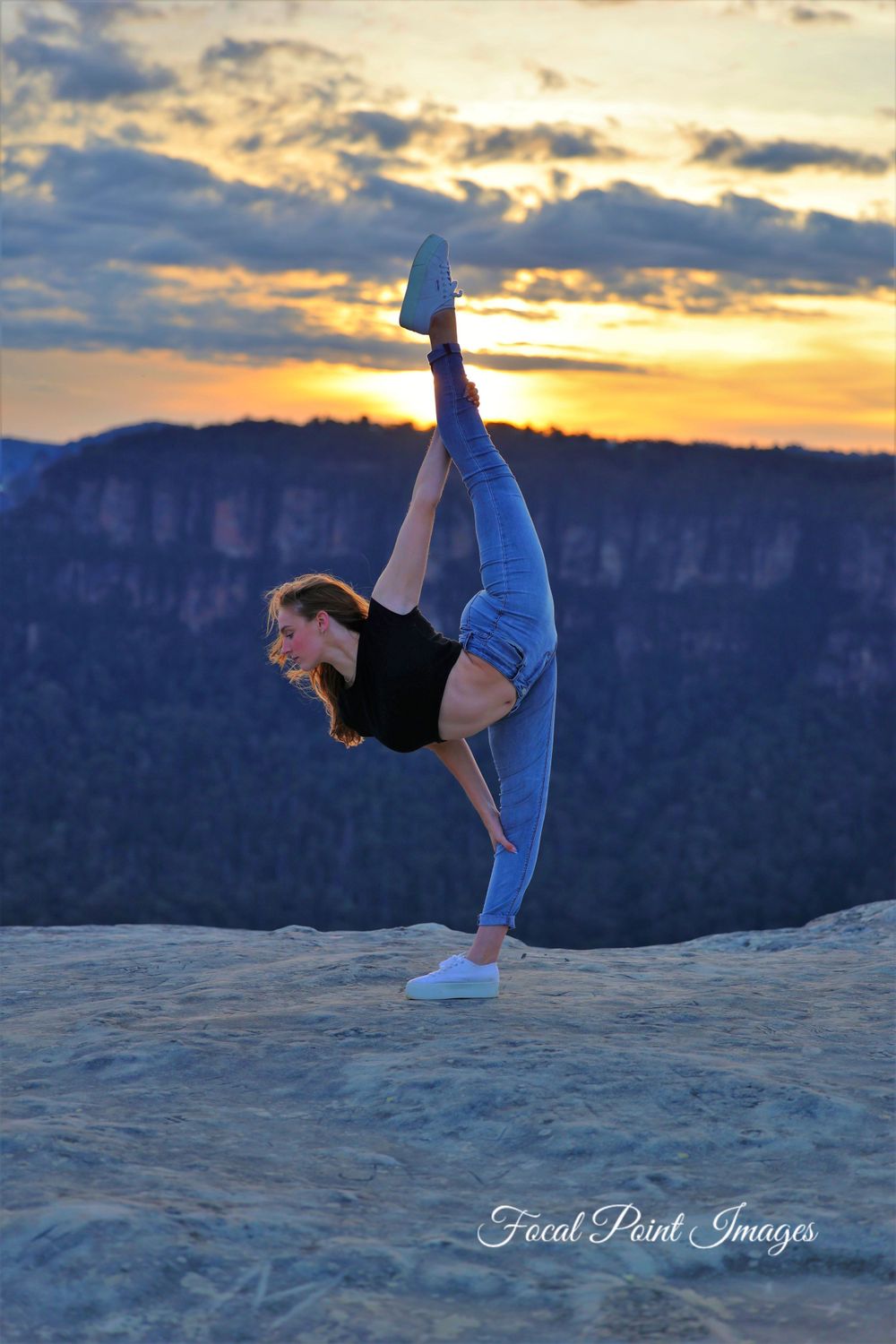 Dancer performs dramatic split pose at sunset on mountain overlook.