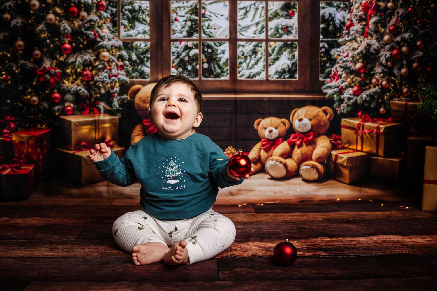 Baby sits with stuffed teddy bears and red Christmas ornaments in festive holiday setting. Christmas mini shoots, Southport