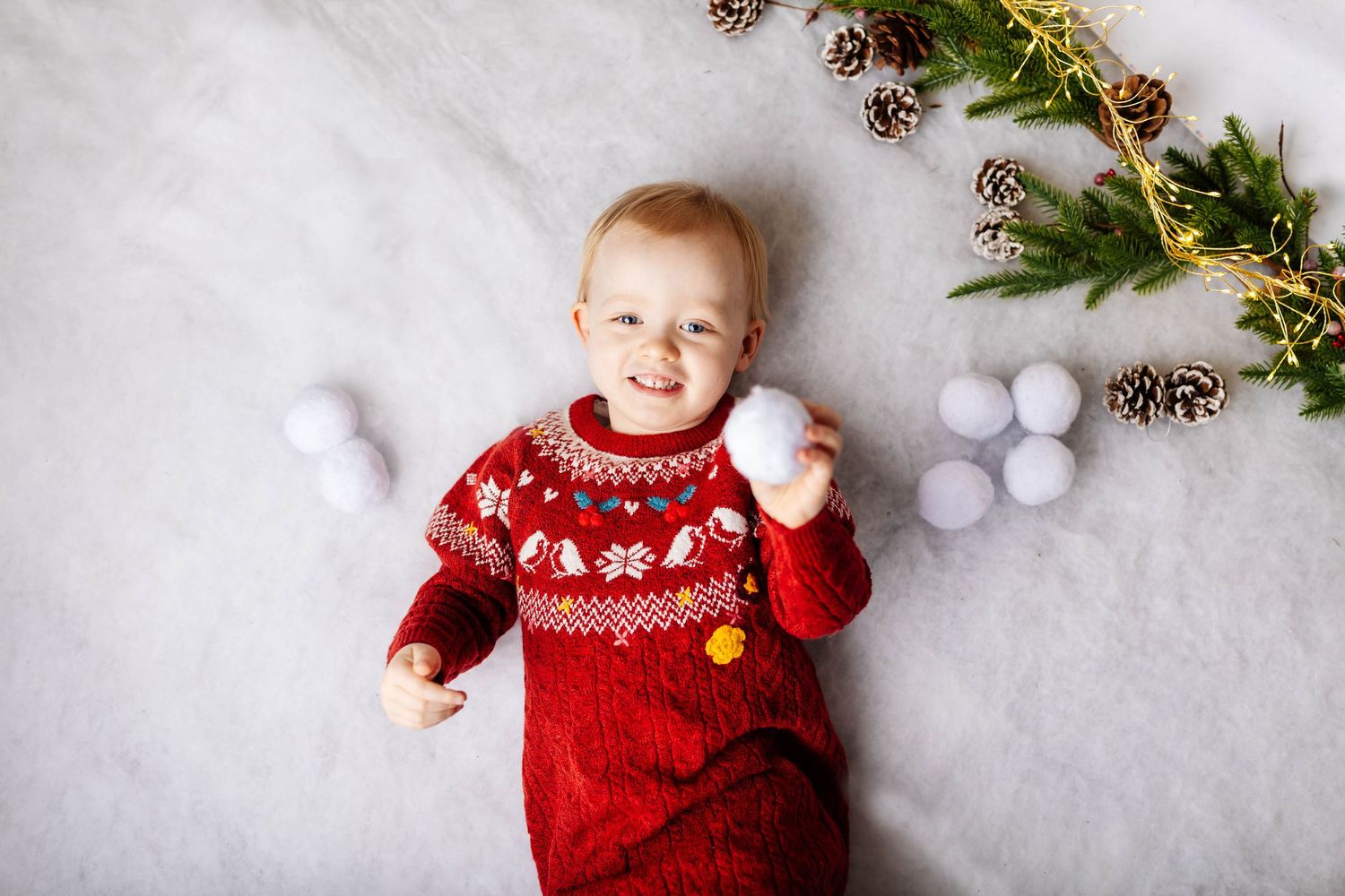 Baby sits with stuffed teddy bears and red Christmas ornaments in festive holiday setting. Christmas mini shoots, Southport