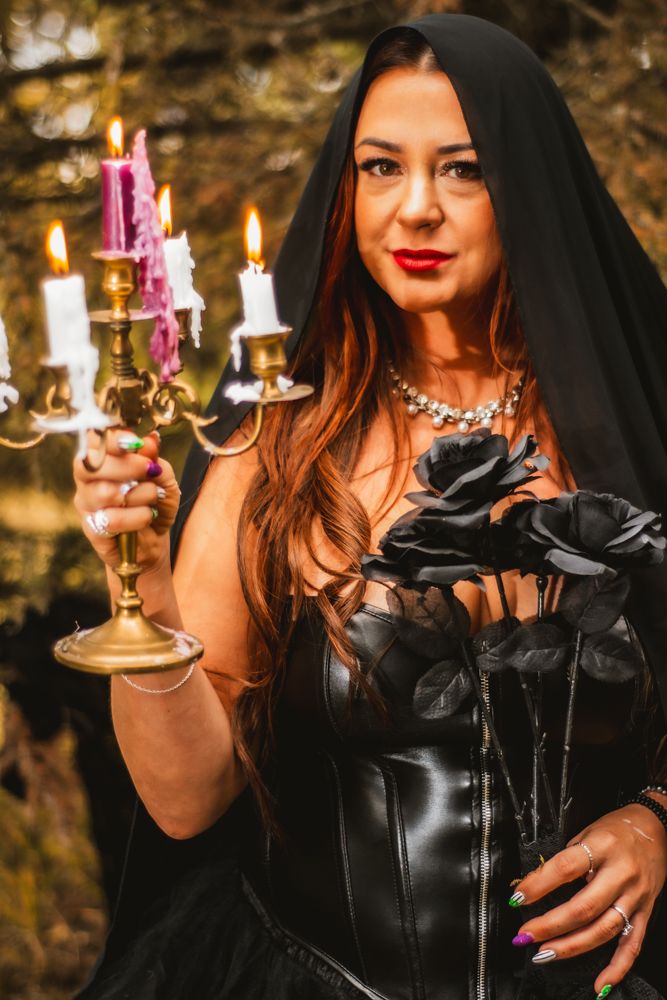 Gothic themed portrait with figure holding candelabra wearing black dress and hooded cape.