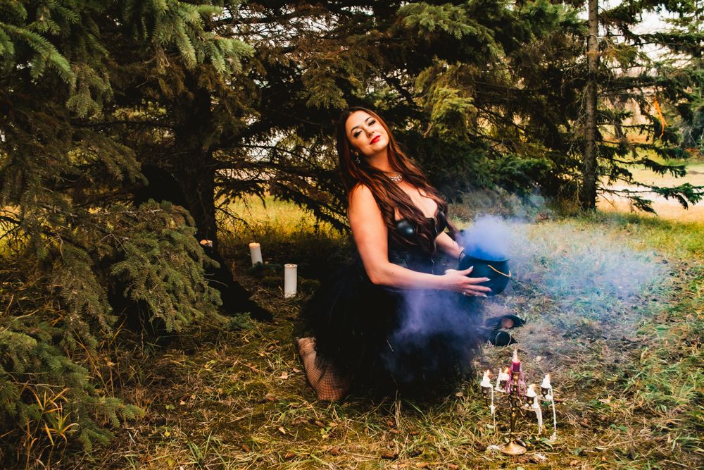Artistic photo of figure in dark tulle dress with smoke effects in forest setting.