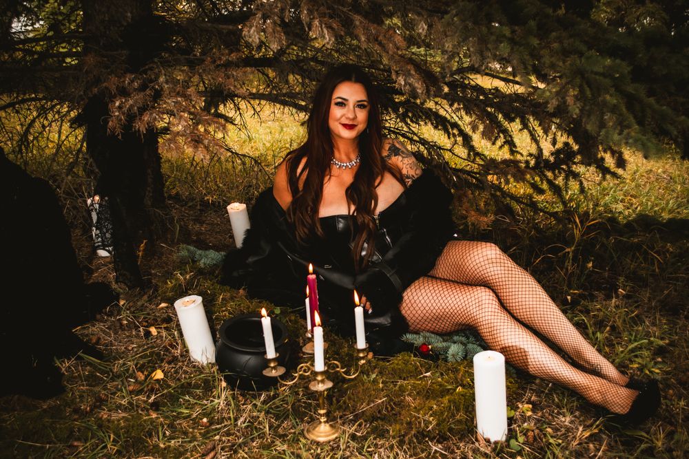 Gothic photoshoot setup with candles and figure reclining in dark dress among trees.