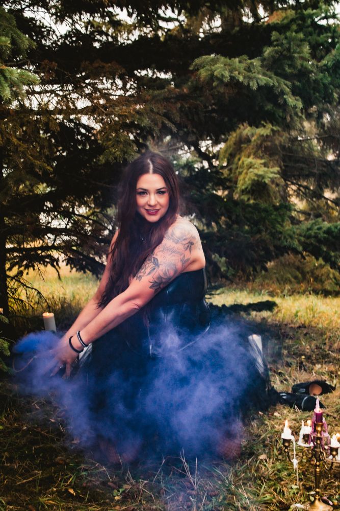 Ethereal forest photoshoot with black dress and blue smoke effects in outdoor setting.