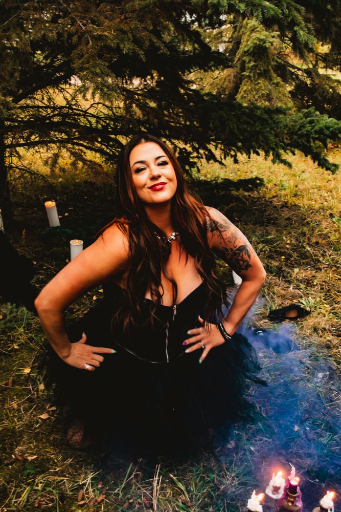 Artistic outdoor portrait with black dress and blue smoke effects against forest backdrop.