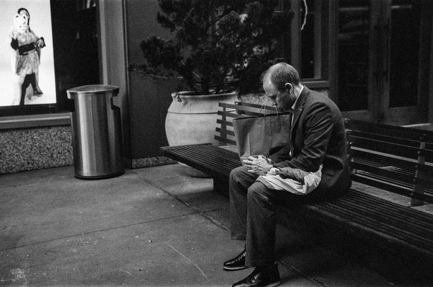Person sitting alone on bench reading newspaper in black and white street photography.