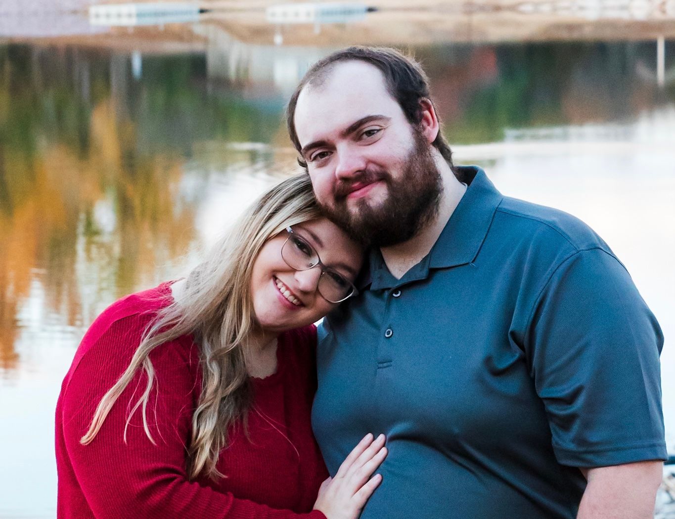 Couple in red and blue sharing an intimate moment by a lakeside during golden hour.