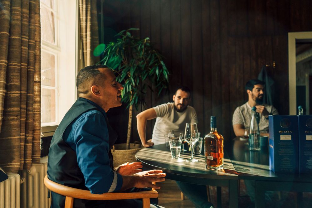 A man sitting in a smoky room with a bottle of metaxa in front of him
