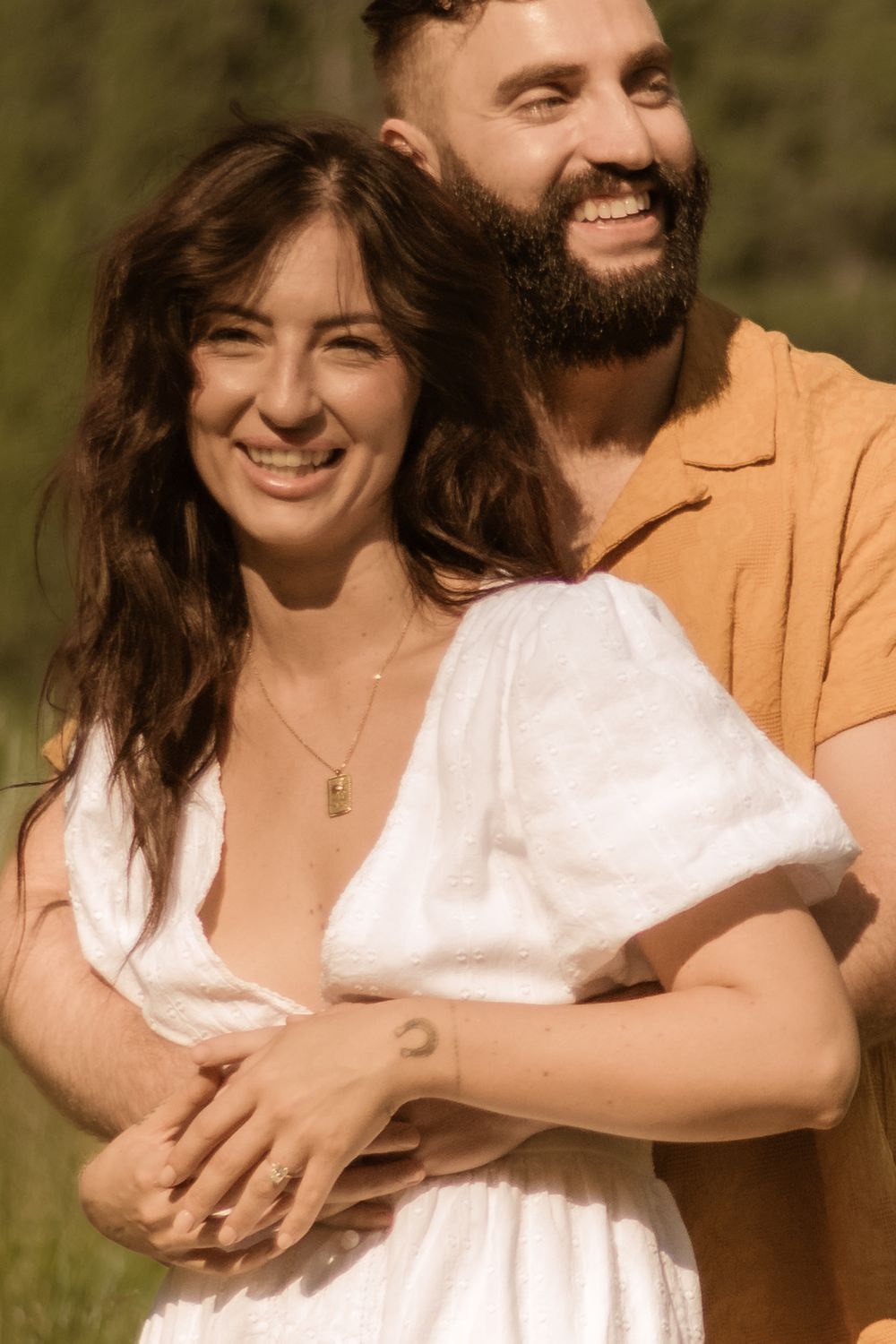 Happy couple shares joyful moments in warm sunlight wearing white dress and mustard shirt.