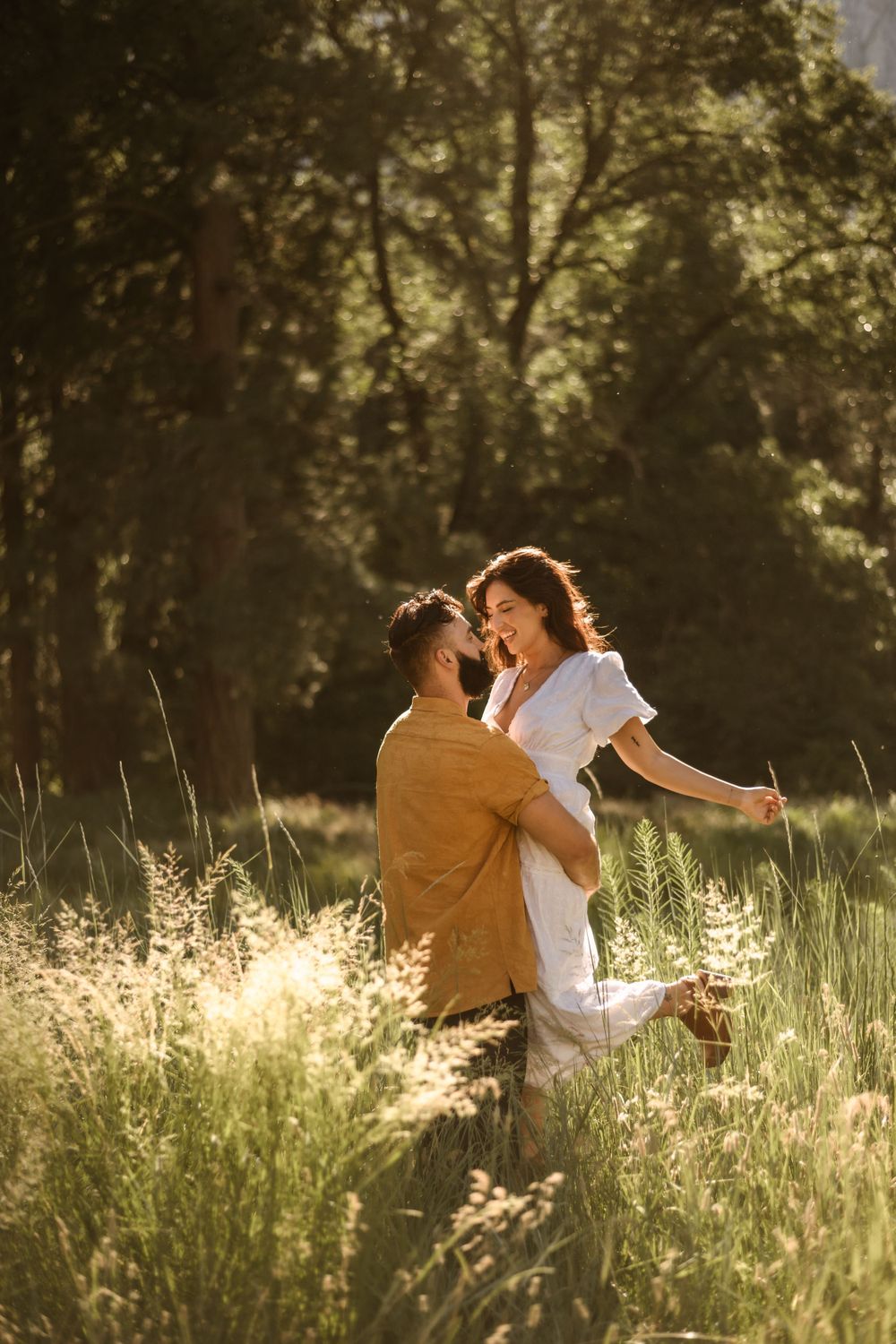 A couple shares a tender moment in tall grass during golden hour sunlight.