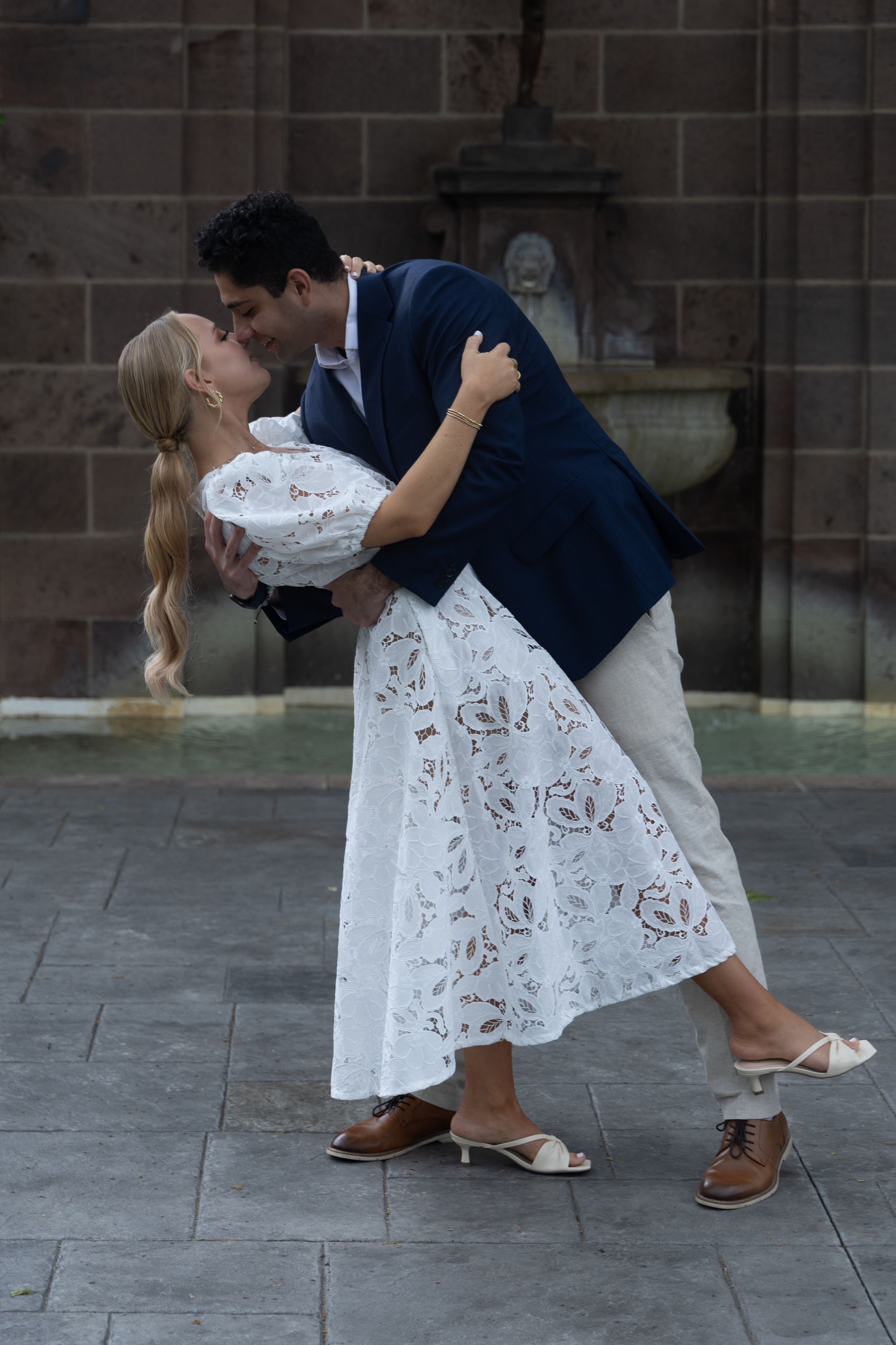 A romantic dance pose with a couple in blue and white attire against a stone wall backdrop.