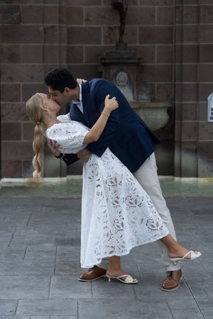 A romantic couple in wedding attire performs a dramatic dip dance pose on a stone patio.