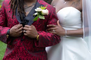 Close-up details of a wedding couple with burgundy and white formal attire holding flowers.