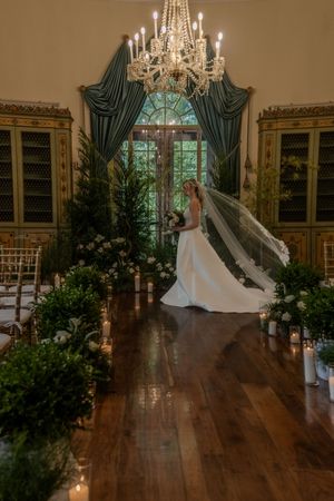 A bridal portrait in an elegant room with chandelier, green drapes, and floral decorations.