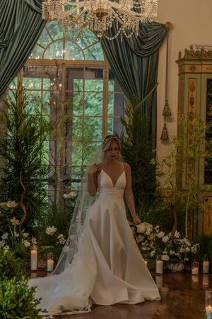 An elegant wedding venue with crystal chandelier, green drapes and evergreen trees decorating the interior space.