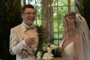 A wedding couple shares a joyful moment in an elegant indoor setting with windows and greenery.