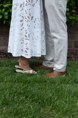 Detail shot of wedding couple's feet on grass, showing white lace dress hem and dress shoes.
